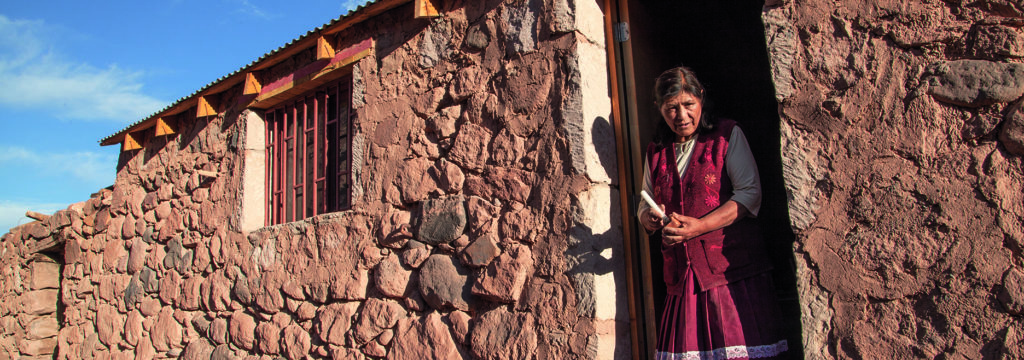 mujer en la puerta de su casa de piedras en una zona desértica, pueblos originarios